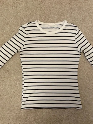 Randig långärmad topp - Vit långärmad topp med svarta horisontella ränder. Klassisk och enkel design med rund halsringning, tillverkad i mjuk bomull.