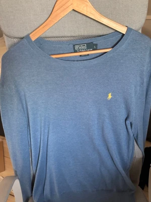 Blå tröja från Polo Ralph Lauren - Snygg blå tröja från Polo Ralph Lauren i slim fit-modell. Tröjan har rund halsringning och den klassiska gula broderade loggan på bröstet. Perfekt för en stilren och avslappnad look. Väldigt bra skick med inga synliga tecken på användning!