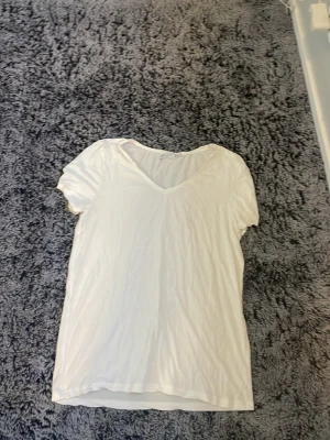 Vit v-ringad t-shirt - En enkel vit t-shirt med v-ringning och korta ärmar. Perfekt basplagg som passar till det mesta. Tillverkad i mjukt material för en skön känsla.