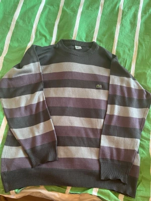 Lacoste tröja L - Snygg tröja från Lacoste med breda horisontella ränder i grått, svart och lila. Strl L.
