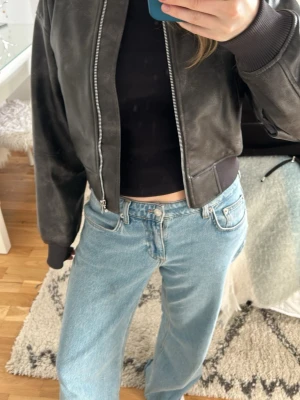 Svart skinnjacka från H&M - Snygg svart skinnjacka från H&M med klassisk bombermodell. Jackan har ribbade muddar vid ärmslut och midja, två snedställda fickor framtill och dragkedja. Perfekt för festivaler och sommaren 