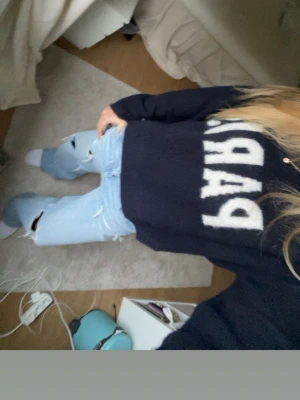 Stickad tröja med text  - Säljer en mörkblå stickad tröja med stort vitt PARIS-tryck på bröstet. Tröjan har en avslappnad passform och långa ärmar. Perfekt för dig som gillar coola statement-plagg och vill ha något mjukt och bekvämt. Jätte gosigt material! 