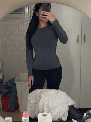 Mörkgrå träningstopp - Slimmad mörkgrå långärmad topp med rund halsringning. Tränings tröjan är stretchigt och bekvämt, perfekt för att skapa en snygg och enkel look. 