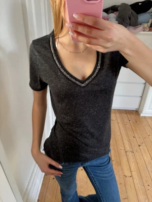 T-shirt med glitterdetalj - Snygg mörkgrå t-shirt med v-ringad hals med glitter. Fint skick, storlek M💕