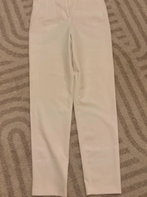 Vita höga kostymbyxor - Stilrena kostymbyxor i vitt med hög midja och raka ben. Byxorna har en minimalistisk design utan synliga detaljer framtill och två fickor bak. Från BGNWorkshop, värda 1000+kr. Sällan använda, men en liten fläck på dem (syns i bilderna)💞