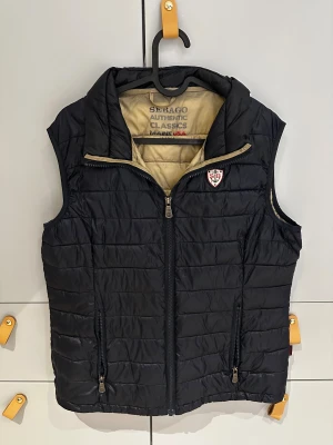 Sebago väst - Lätt och varm quiltad väst från Sebago – Authentic Classics. Perfekt som mellanlager eller som ytterplagg på vår och höst. Flera fickor, hög krage och tidlös design. Bra använd skick utan defekter. Funkar även för storlek M personer.