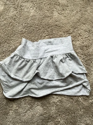 Grå volangkjol  - Supersöt grå kjol med bred resår i midjan och dubbla volanger. Kjolen är gjord i mjukt material och har en avslappnad, lite basic vibe. Perfekt för dig som gillar bekväma men ändå snygga plagg. Är i barn stolek och är som nytt och använt ungefär bara en gång.