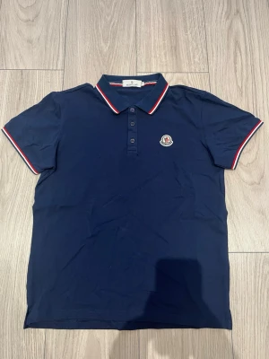 Marinblå pikétröja från Moncler - Klassisk mörkblå pikétröja frän Moncler i nytt skick. Köpt på plick så kan ej garantera äkthet. Priset är inte hugget i sten, bara att skriva vid frågor.
