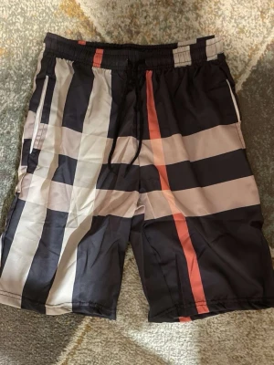 Rutmönstrade shorts med snörning - Snygga shorts med klassiskt rutmönster i svart, beige och rött. Shortsen har elastisk midja med snörning och sidofickor. Perfekta för sommaren och har en loose passform som ger en avslappnad stil.