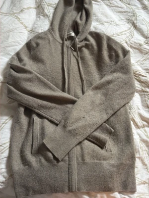 Soft goat hoodie - Säljer en hoodie med dragkedja och huva från soft goat i cashmir. Tröjan har ribbade muddar vid ärmslut och nederkant samt två fickor framtill. Perfekt för en chill och stilren look. Sparsamt använd men något nopprig vid armhålan och armarna. Storlek S, färg: greige. Nypris: 2800kr. Hör av dig vid fler frågor!