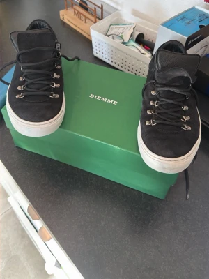 Svarta Diemme sneakers med mocka - Snygga svarta sneakers från Diemme i mocka med vita sulor och metallöglor för snörningen. Skorna har en klassisk låg profil och robust känsla, perfekta för dig som gillar stilrena och tidlösa sneakers. Diemme-logga syns på innersulan.