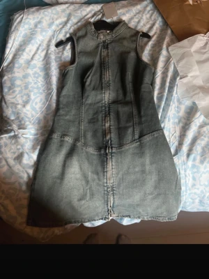 Ärmlös jeansklänning i denim - Säljer en snygg ärmlös jeansklänning i tvättad blå denim. Klänningen har hög krage, knappdetalj vid halsen och markerade sömmar framtill för en cool look.