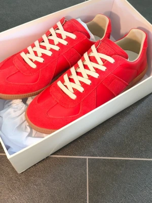 Röda GATS från Maison Margiela German army trainers - Snygga röda sneakers från Maison Margiela med ovandel i mocka och läder, vita bomullssnören och klassisk gummisula. Ikonisk design med diskret logotyp på plösen. Perfekta för dig som vill sticka ut med stilrena detaljer och trendig färg.
