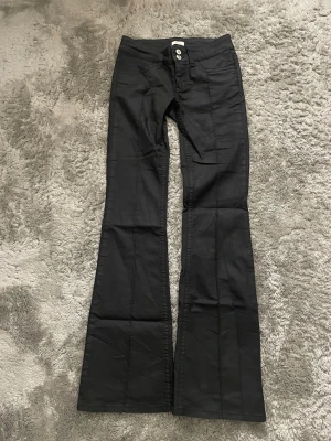 Svarta bootcut skinn jeans från Nelly - Svarta jeans med bootcut-modell. Jeansen har utsvängda ben och synliga sömmar. Skinn material eller vad man ska kalla det för. Använda två gånger men har en liten fläck, inget som syns mycket.