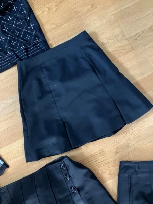 Svart kortkjol i stilren design - Enkel och stilren svart kortkjol med lätt utsvängd form. Kjolen har en slät framsida utan synliga detaljer och passar perfekt till många olika outfits.