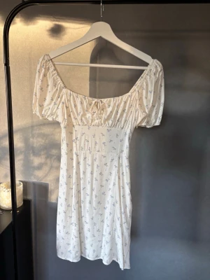 Vit blommig kortklänning - Supersöt vit kortklänning med små blå blommor, puffärmar och smock i ryggen 💞