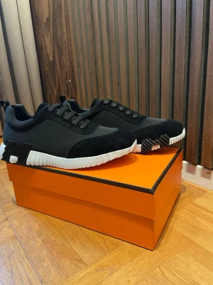 Svarta H märkes skor med vit sula - Snygga svarta sneakers från H med cool design och kontrasterande vit sula. Skorna har ovandel i mesh och mockadetaljer, samt svarta skosnören. Perfekta för dig som vill ha en stilren och exklusiv look.