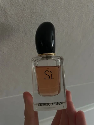Giorgio Armani Sì Eau de Parfum 30ml - Giorgio Armani Sì Eau de Parfum i en elegant glasflaska med svart lock och guldiga detaljer. Parfymen har en mjukt rosa nyans och flaskan är stilren med märkets logga framtill. Perfekt för dig som gillar lyxiga och feminina dofter.             Nypris kostar 750kr 30 ml 