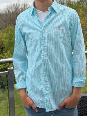 Randig blå skjorta från Polo Ralph Lauren - Snygg blå- och vitrandig skjorta från Polo Ralph Lauren med klassisk krage och lång ärm. Skjortan är i mycket fint skick, inte använd mycket alls. Sitter som en smäck, skriv vid minsta fundering🙌🏻🙌🏻