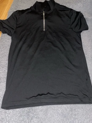 Svart t-shirt med Florida-tryck - Cool svart t-shirt med färgglatt tryck på ryggen som visar palmer och texten 'FLORIDA Atlantic'. Framsidan har en half zip-dragkedja vid halsen. Perfekt för dig som gillar streetstyle och grafiska motiv. 300 kr st 
