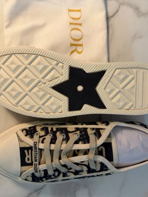 Dior låga sneakers Walk’n’dior 38 - Walk’n’dior/ Snygga låga sneakers från Dior med klassiskt blått och vitt Oblique-mönster. Skorna har vita snören, gummisula med stjärndetalj och tydlig Christian Dior-logga på plösen. Tillverkade i canvas och gummi för en trendig och exklusiv look.