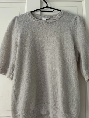 Beige stickad tröja från Name It - Säljer en stilren beige stickad tröja från Name It med rund halsringning och halvlånga ärmar. Tröjan har en mjuk och skön känsla, perfekt för lager-på-lager och enkel att matcha med olika outfits.