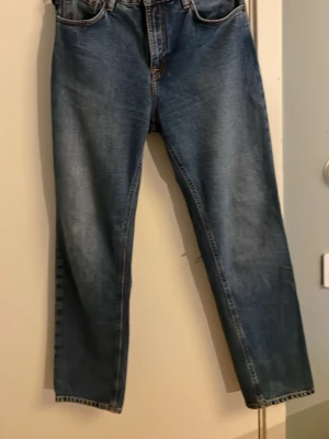 Blå raka jeans från Nudie Jeans - Säljer ett par klassiska blå jeans från Nudie Jeans med rak passform och normal midja. Jeansen har  Nudie Jeans signaturbroderi på bakfickorna. Perfekta till en avslappnad stil och enkel att ha på sig i vardagen