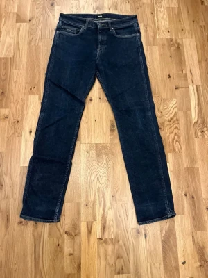 Mörkblå raka jeans från boss - Snygga mörkblå jeans från Boss med klassisk rak passform och fyra fickor. Jeansen har diskreta kontrastsömmar och en läderpatch bak i midjan. Perfekta för en stilren och avslappnad look.