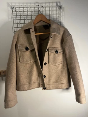 Beige kappa med stora fickor - Stilren beige kappai ullmix med klassisk krage och svarta knappar. Två stora bröstfickor med lock och knapp framtill. Rak passform och långa ärmar, perfekt för lager-på-lager. Enkel och trendig design som passar till många outfits.💕💕