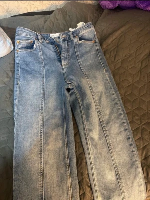 Ljusblå raka jeans med pressveck - Säljer ett par ljusblå jeans med raka ben och markerade pressveck framtill. Jeansen har råa, fransiga benslut och klassisk femficksdesign. Perfekta för en trendig och avslappnad look. Materialet är denim i bomull.