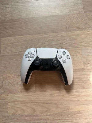 Sony DualSense PS5 handkontroll vit - Säljer en vit och svart Sony DualSense handkontroll till PlayStation 5. Kontrollern har en modern design med touchpad, inbyggd mikrofon och adaptiva triggers. Tillverkad i plast och passar perfekt för gaming på PS5.