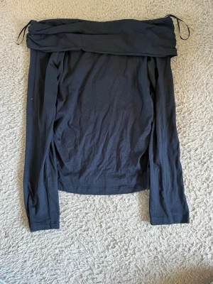 Svart offshoulder topp Gina Tricot - Svart långärmad offshoulder topp från Gina Tricot. Toppen har en snygg draperad kant upptill och är tillverkad i mjuk bomull. Perfekt för dig som gillar en stilren och trendig look.