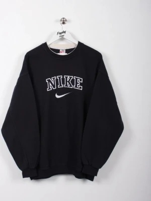 Svart stickad sweatshirt från Nike - Svart stickad sweatshirt från Nike med klassisk logga och vit text framtill. Tröjan har rund halsringning, långa ärmar och ribbade muddar vid ärmslut och nederkant. Perfekt för en avslappnad och sportig stil.