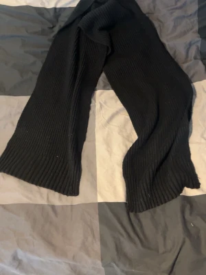 Svart ribbstickad halsduk - En lång svart halsduk i ribbstickat material. Den är mjuk och enkel att matcha med olika outfits. Perfekt för att hålla värmen under kyliga dagar och har en klassisk, stilren look.