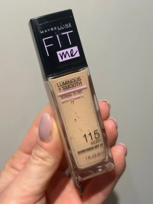 Maybelline Fit Me Foundation 115 Ivory - Maybelline Fit Me Luminous + Smooth foundation i nyansen 115 Ivory. Flytande foundation för normal till torr hud, med vitamin E och SPF 18. Kommer i en rektangulär glasflaska med svart plastlock. Ger en naturligt fräsch finish. Använd endast 1-3 gånger 