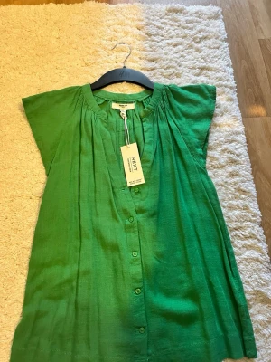 Grön linnetopp från Next - Snygg grön blus från Next i luftigt linnematerial. Modellen har knappar framtill, rundad halsringning och korta ärmar. Perfekt för dig som gillar en avslappnad men ändå trendig stil. Enkel att matcha med både jeans och kjol.