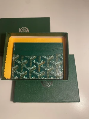 Grön kortfodral från Go4yard - Snyggt grönt kortfodral från Go4yard med det klassiska mönstret i vitt och svart. Tillverkad i tåligt canvasmaterial med läderdetaljer. Fodralet har flera kortfack och kommer i originalask med gul putsduk.