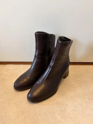 Bruna ankelboots från XIT – storlek 37 - Bruna ankelboots från XIT – storlek 37  Säljer ett par stilrena och bekväma ankelboots från XIT i storlek 37. Klassisk mörkbrun färg som passar till det mesta – perfekta både till vardag och jobb. 	•	Låg, stabil klack (bekväma att gå i hela dagen) 	•	Dragkedja på sidan för enkel av- och påtagning 	•	Mjukt material med fin passform 	•	Diskret och tidlös design  Skorna är använda men i fint skick (se bilder). Sulorna har normalt slitage men mycket kvar att ge.  Perfekta höst- och vårskor! 