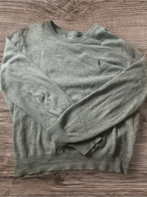  Polo Ralph Lauren Stickad Tröja Grå Merinoull - Säljer en stilren och tidlös gråmelerad tröja från Polo Ralph Lauren i 100% exklusiv merinoull.  • Tröjan är i mycket bra begagnat skick. Inga hål, fläckar eller andra defekter. Den mörkblåa signaturponnyn är snyggt broderad på bröstet. Garanterat äkta. • Mått: • Bröstvidd (Armhåla till armhåla): 56 cm • Längd (Axel och nedåt): 60 cm • Ärmlängd: ca 50 • Material: 100%