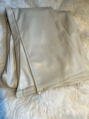 Beiga vida byxor i fuskskinn - Säljer ett par snygga byxor i beige fuskskinn med utsvängda ben. Byxorna har hög midja och slät framsida utan fickor. Väldigt stretchiga och sköna.