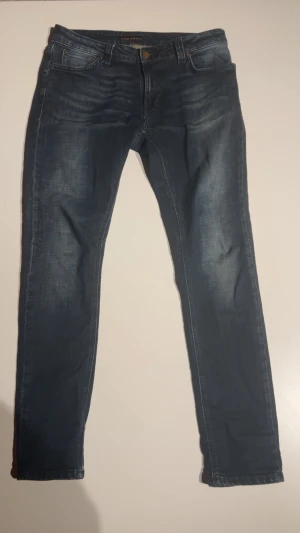 Mörkblå från Nudie - Snygga mörkblå jeans från Nudie med klassisk femficksdesign. Jeansen har en smal passform perfekt för grisch stilen. Det är tillverkade i bomull med stretch för extra komfort. Perfekt för dig som gillar en modern och stilren look.