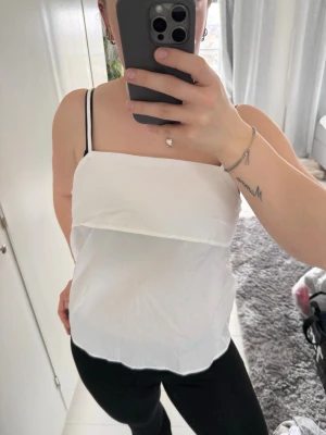 Vit ärmlös linnetopp med smala band - Säljer en enkel och stilren vit linnetopp med tunna axelband. Toppen har rak skärning och är lätt och luftig, perfekt för varma dagar. Passar till både jeans och kjol för en clean look.