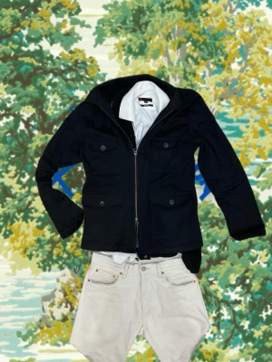 John Henric Overshirt  - Svart overshirt från John Henric med rak passform, fyra stora fickor med lock och knapp, samt dragkedja framtill. Klassisk krage och stilren look. Materialet är kraftigt och ger en clean vibe, perfekt att bära över en t-shirt eller skjorta.