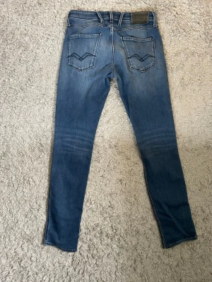 Blå jeans från Replay W30 L32 - Säljer ett par blå jeans från Replay med klassisk femficksmodell. Jeansen har normal midja, smal passform och stretchigt material för extra komfort. Bakfickorna har Replay’s karaktäristiska sömmar. Läder loggan över backfickan är lite lös men går att sy fast igen, st W30 L32