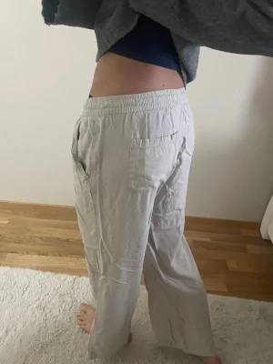 Beiga vida linnebyxor med resår - Säljer ett par beiga linnebyxor med avslappnad passform och resår i midjan. Byxorna har raka ben, sidofickor och en bakficka. Perfekta för en chill och stilren look. Materialet är tunt och luftigt linneblandning.