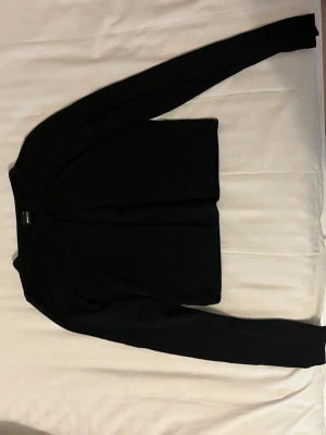 Svart enkel kofta - Stilren svart kofta med rund halsringning och långa ärmar. Koftan har en rak passform och stängs framtill med en knapp.