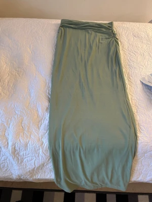 Ljusgrön långkjol i mjukt tyg - Snygg ljusgrön långkjol med enkel och rak passform. Kjolen har en lätt drapering upptill och är gjord i ett mjukt, stretchigt material som känns skönt mot huden. Perfekt för dig som gillar en avslappnad men ändå stilren look.