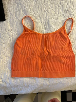 Ribbad orange linnetopp - Snygg ribbad orange linnetopp med smala axelband. Perfekt för varma dagar och enkel att styla med jeans eller kjol. Toppens material är mjukt och stretchigt för en bekväm passform.