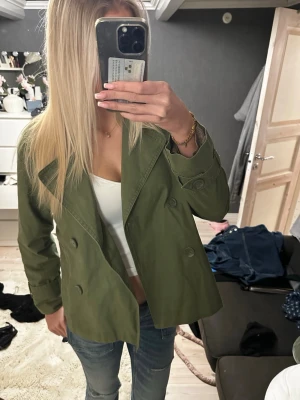 Grön dubbelknäppt jacka - Stilren grön jacka med dubbelknäppning och bred krage. Jackan har en loose passform och är tillverkad i bomull, perfekt för lager på lager. Passar till jeans och crop top för en avslappnad look.