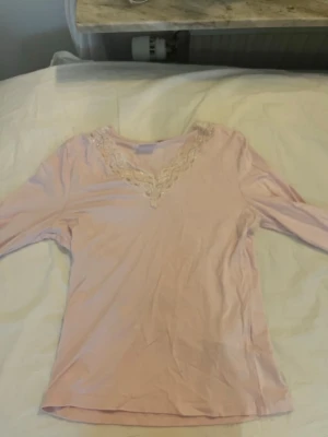 Ljusrosa topp med spets från Gina Tricot - Supersöt ljusrosa topp från Gina Tricot med v-ringning och spetsdetaljer runt halsen. Toppen har lång ärm och är gjord i ett mjukt material som känns skönt mot huden. Perfekt att styla med jeans eller kjol för en feminin look.